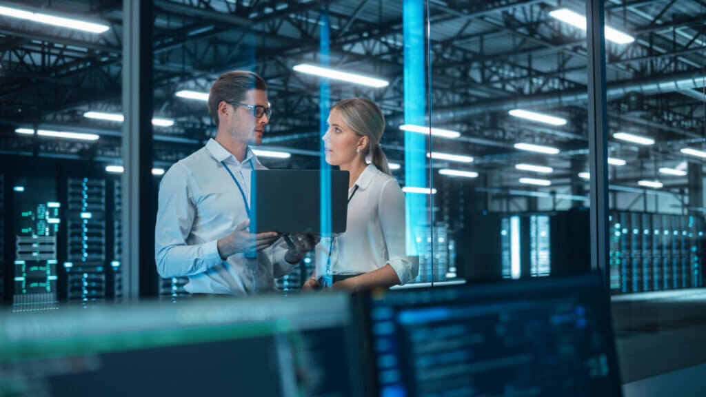 Oil & Gas 1 Two professionals discussing work in a data center with glowing servers in the background.
