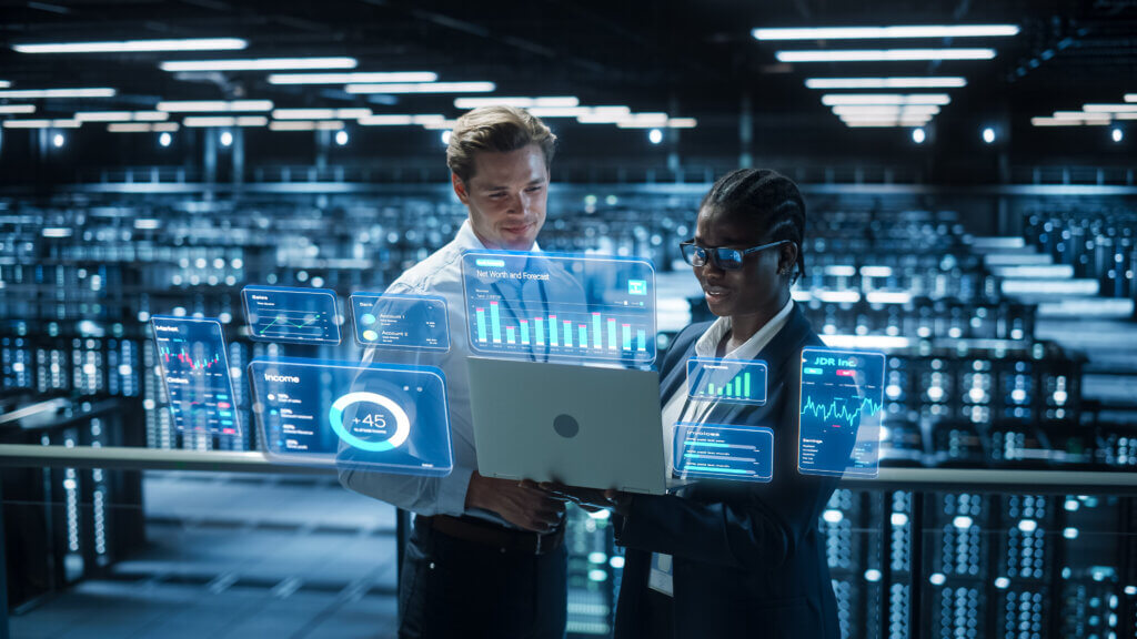 Hyperscalers 1 Two professionals reviewing business data and analytics on a laptop in a modern data center with glowing digital displays.