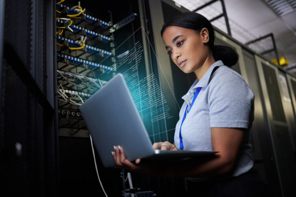 Cloud 1 A woman standing in front of server racks, typing on a laptop, with network cables visible in the background.