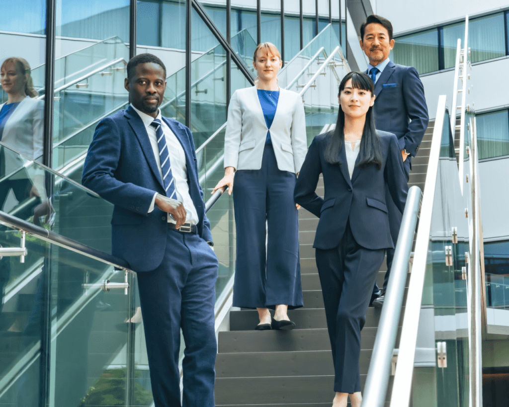 Group of four business professionals walking down a staircase in a modern office building, dressed in formal business attire.